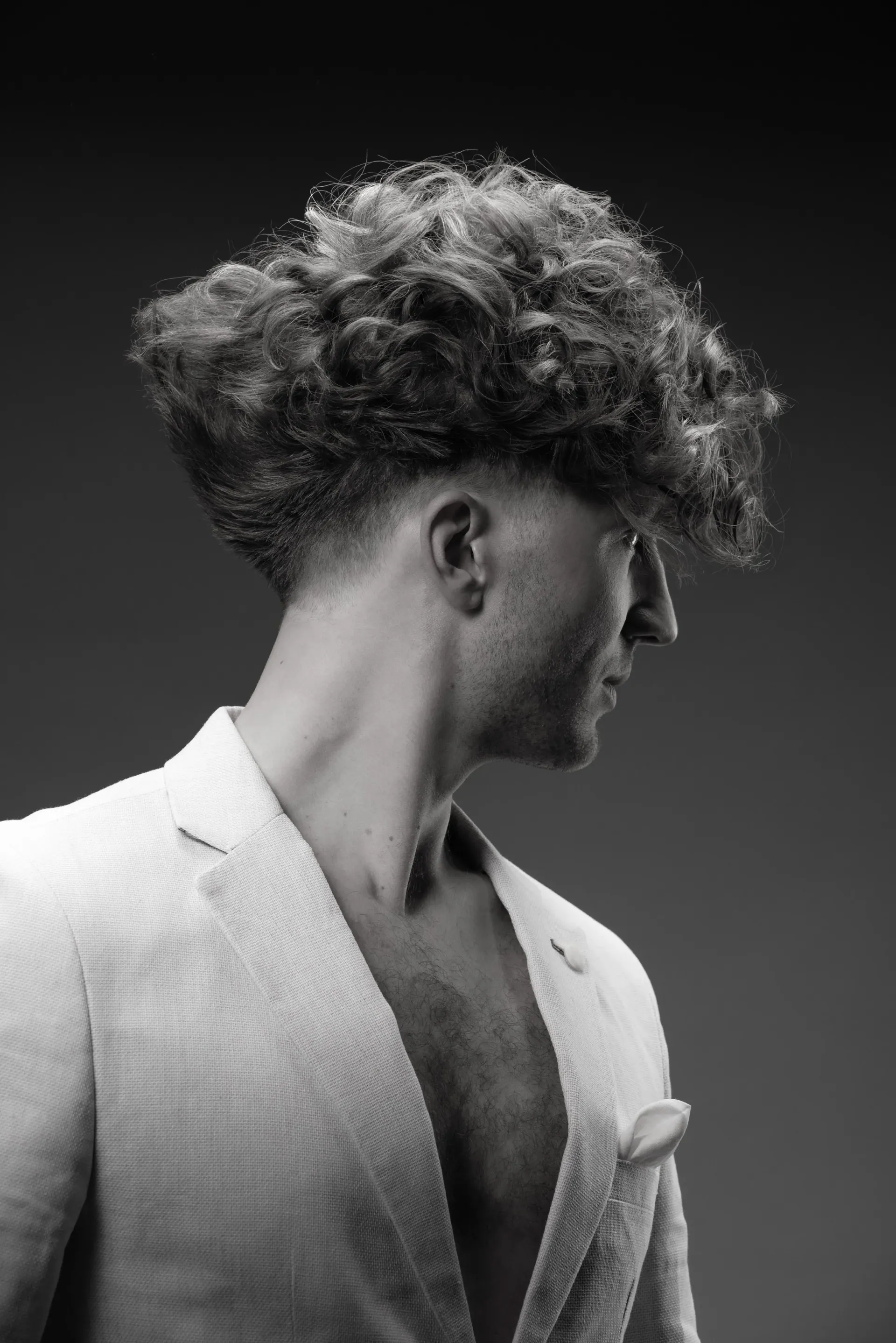 Svartvit bild av en man i profil med stort, lockigt hår och öppen vit blazer